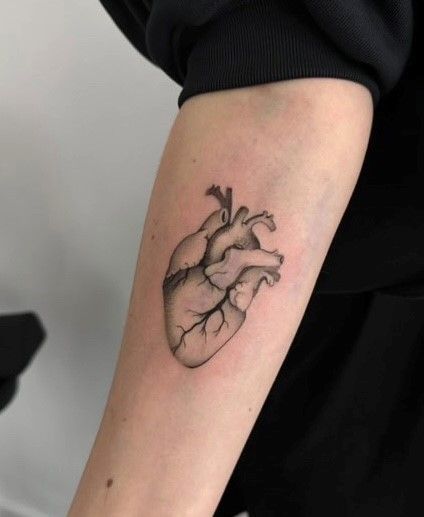Eine schwarz-weiße Tätowierung eines menschlichen Herzens auf dem Unterarm einer Person.
