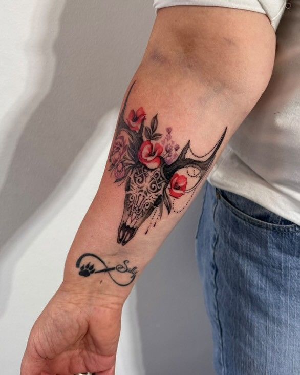 Eine Frau hat ein Tattoo eines Hirschschädels mit Blumen auf ihrem Unterarm