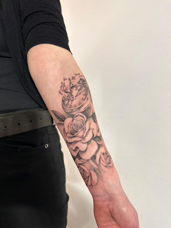 Eine Frau hat eine Tätowierung aus Rosen und einem Herzen auf ihrem Unterarm.
