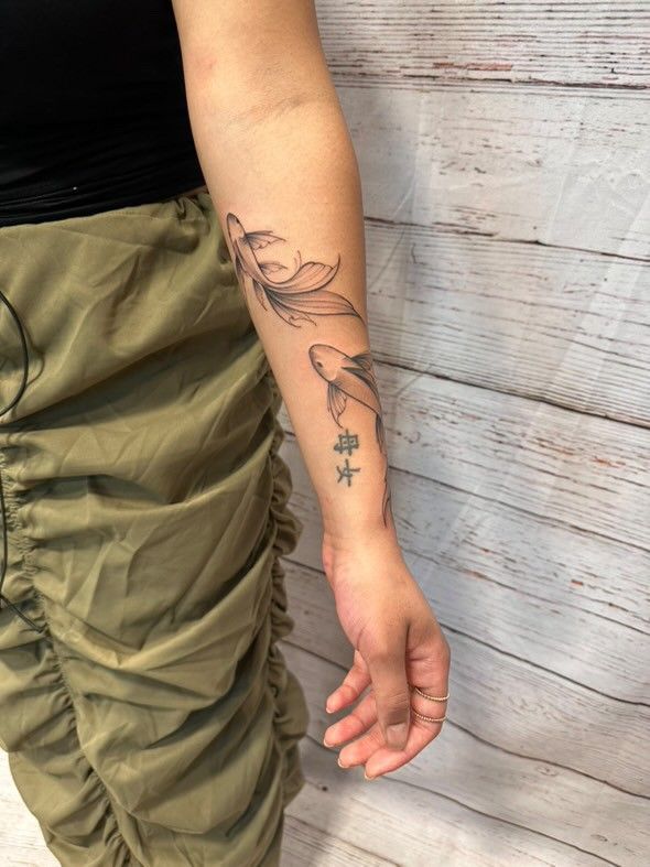 Eine Frau hat eine Fischtätowierung auf ihrem Unterarm.