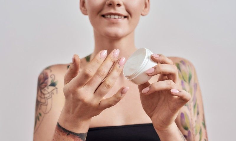 Frau mit frischem Tattoo trägt Creme auf für eine ideale Tattoo Pflege nach dem Stechen
