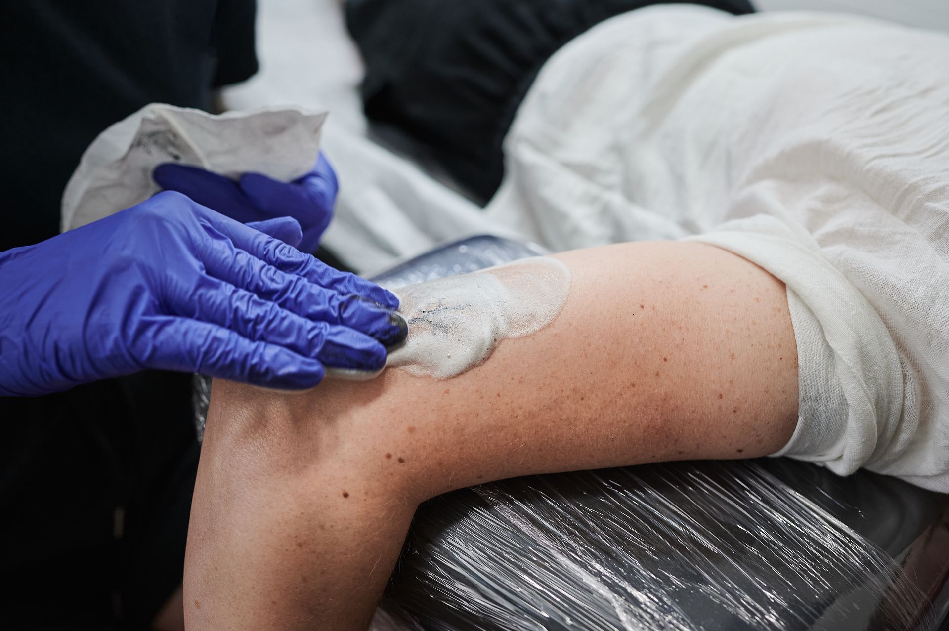 Frau mit frischem Tattoo bekommt Creme aufgetragen für eine ideale Tattoo Pflege nach dem Stechen Frau mit frischem Tattoo bekommt Creme aufgetragen für eine ideale Tattoo Pflege nach dem Stechen