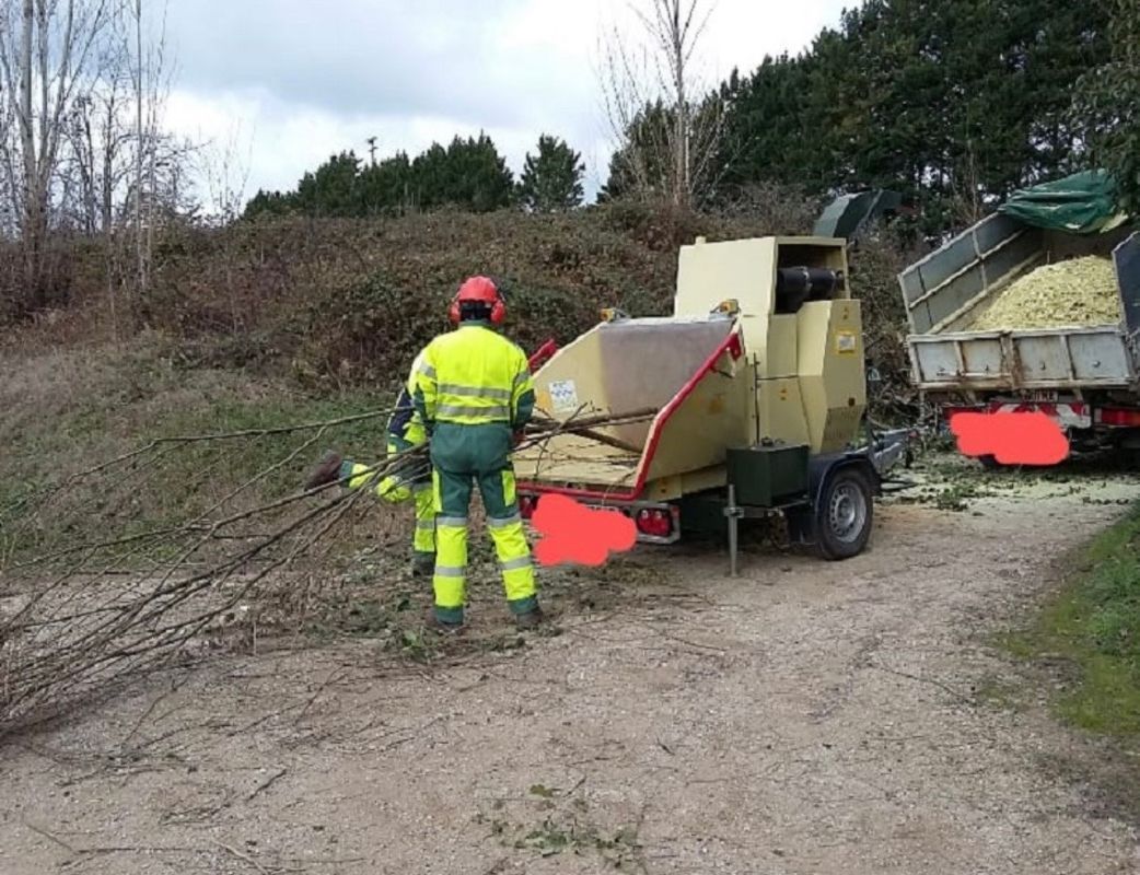 Un ouvrier en tenue de sécurité fluo se tient près d’un broyeur de branches sur un chemin de terre