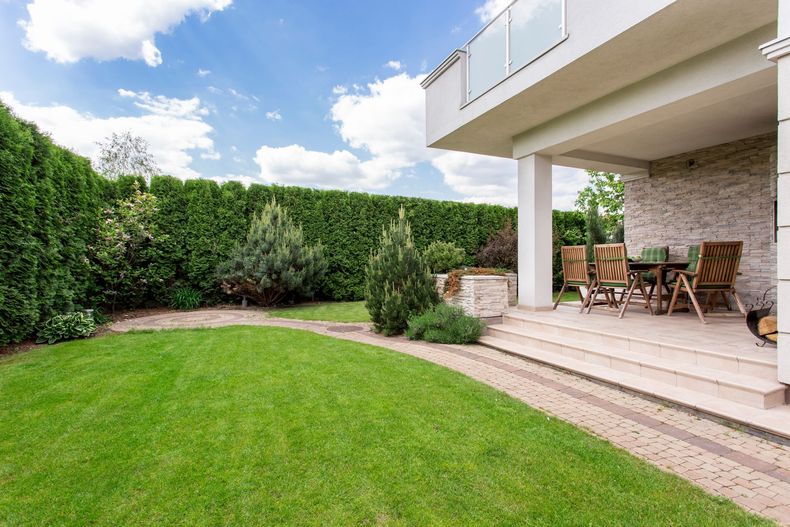 Patio moderne dans un jardin avec des chaises et une pelouse verdoyante bordée de hautes haies