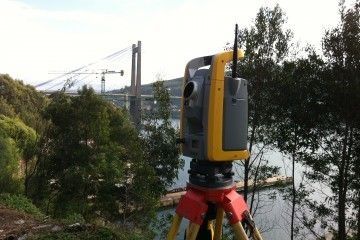 Un dispositivo amarillo y negro está sentado sobre un trípode frente a un puente.