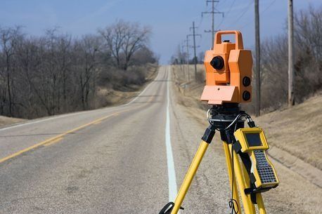 Un teodolito naranja está sentado sobre un trípode al costado de una carretera.