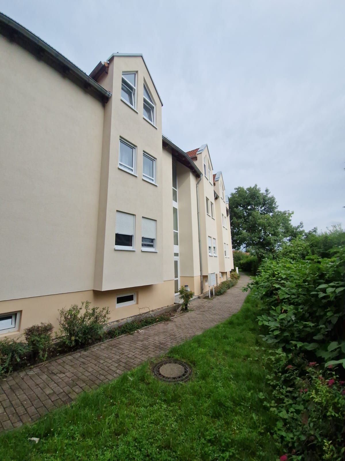 Mehrfamilienhaus mit heller Fassade und Dachgauben unter bewölktem Himmel