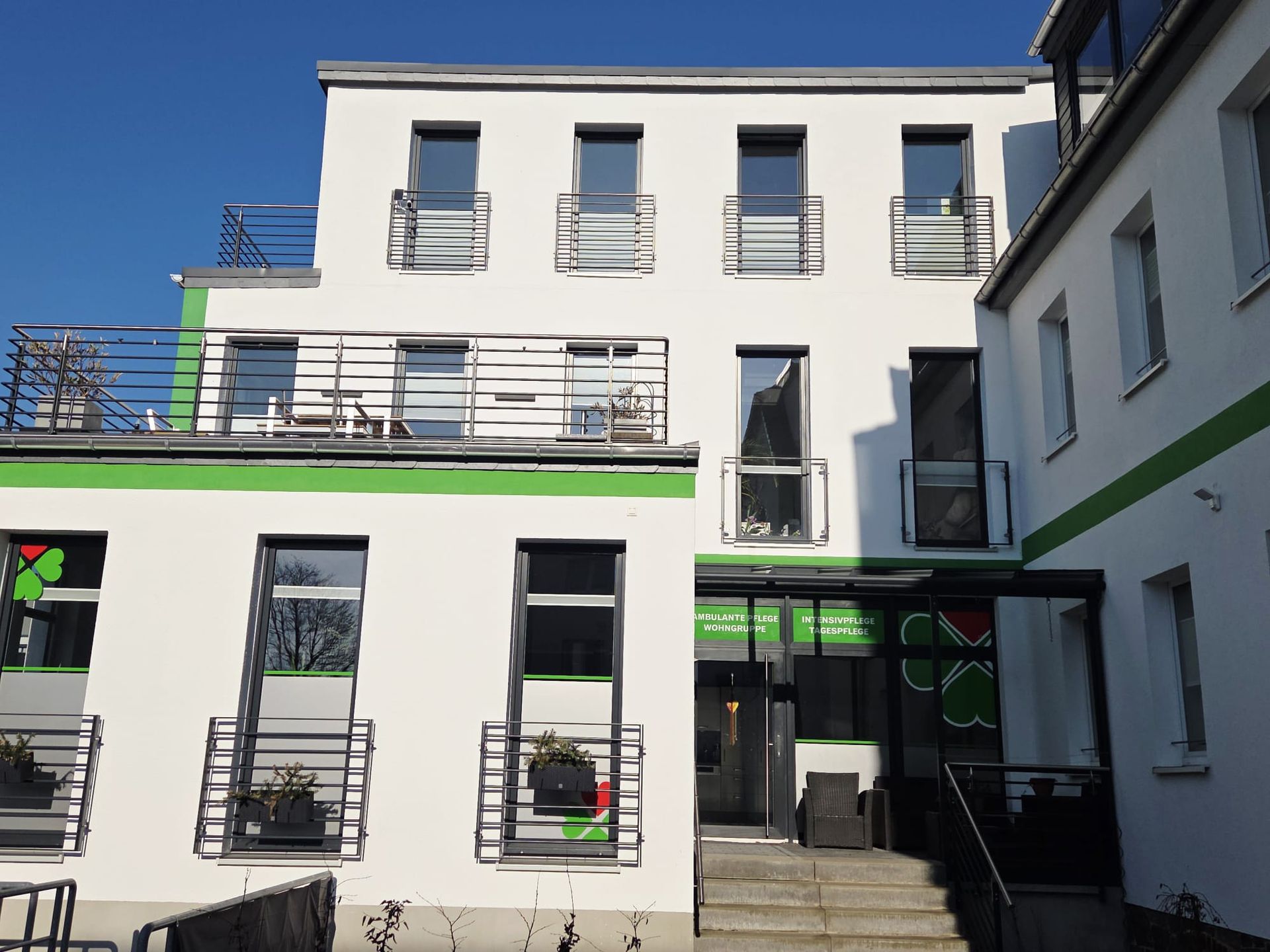Modernes Pflegegebäude mit weißer Fassade und grünen Akzenten unter blauem Himmel