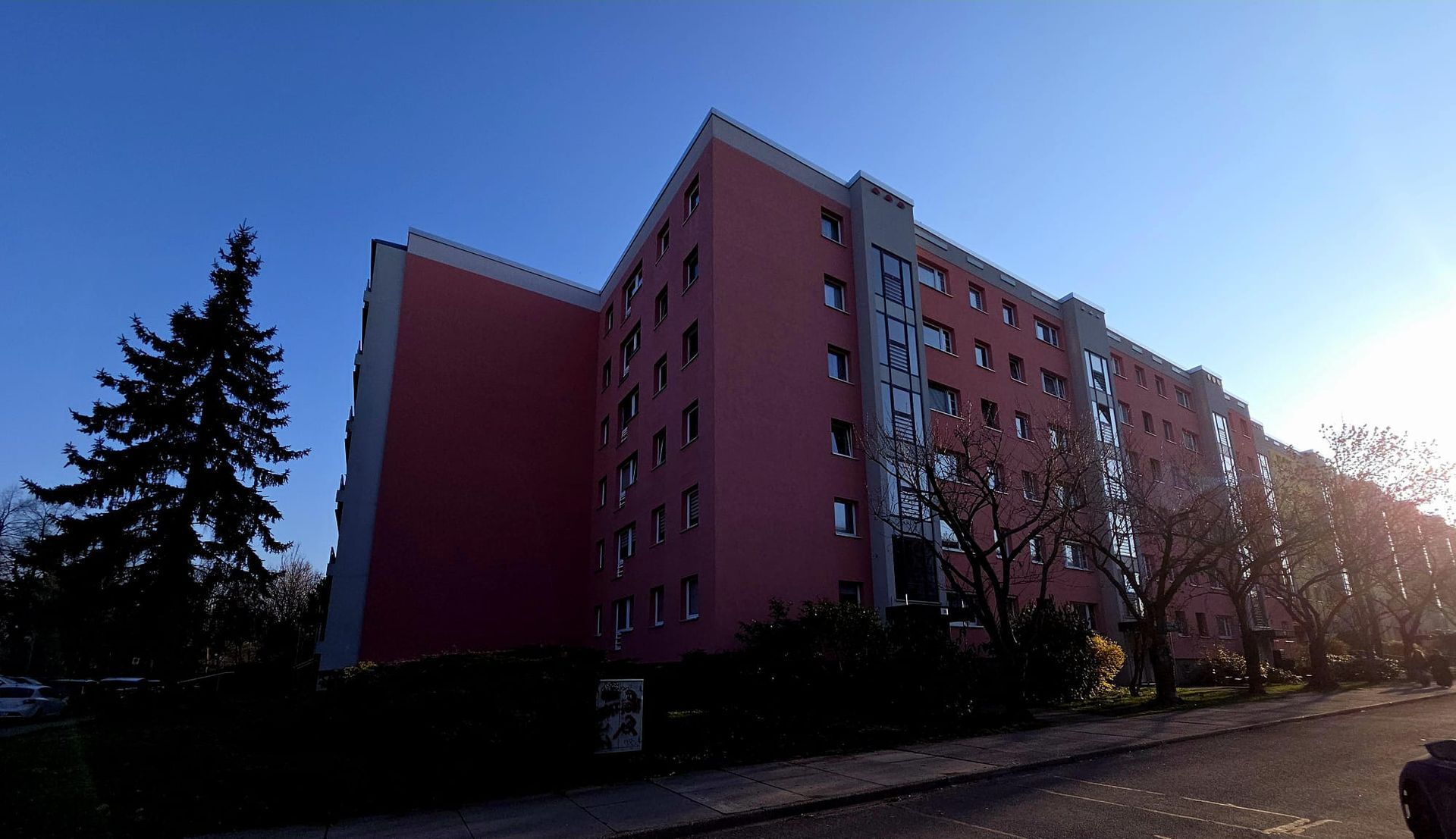 Mehrstöckiges Wohngebäude mit roter Fassade und Balkonen im Sonnenlicht