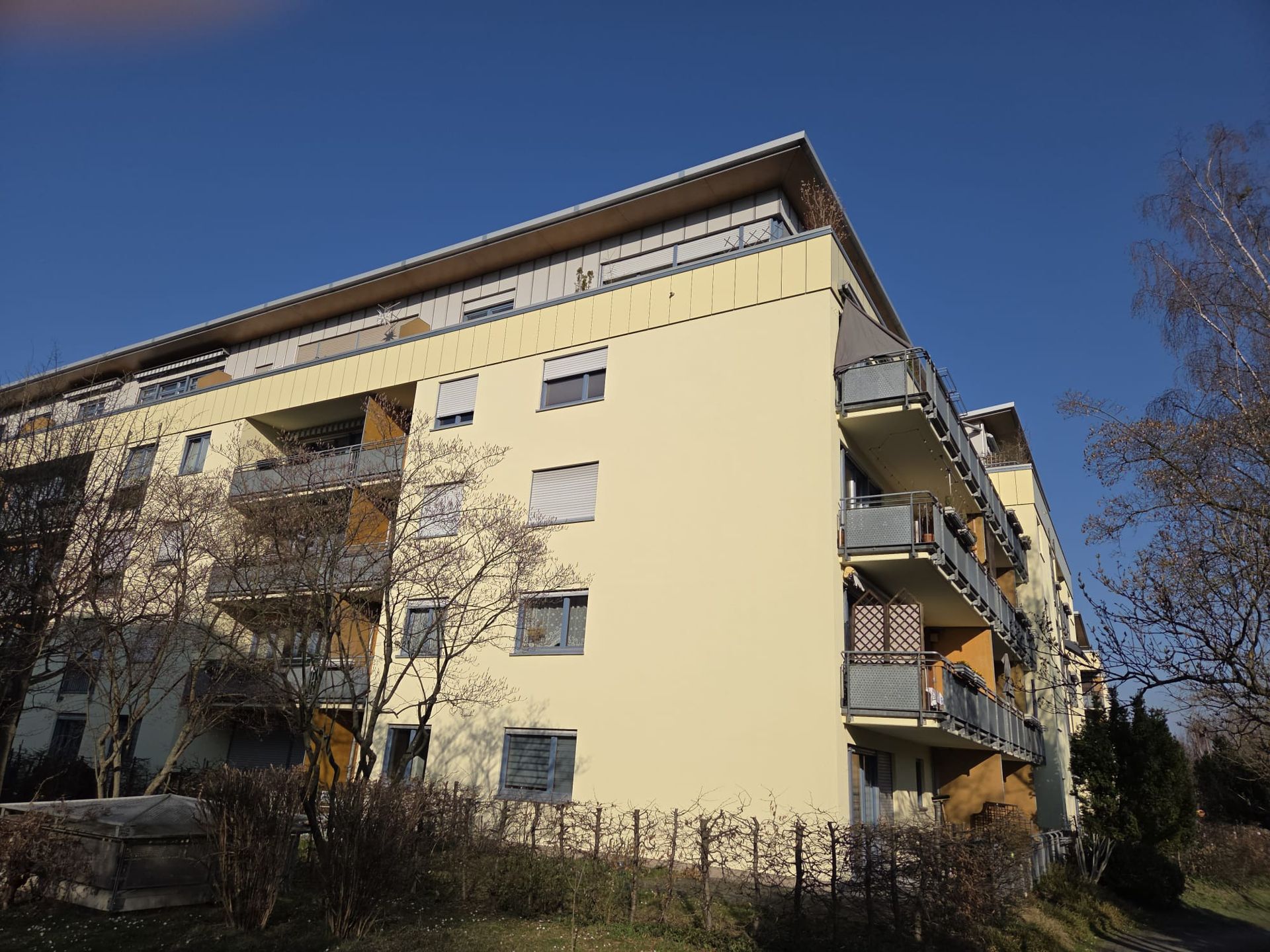 Wohngebäude mit Balkonen und heller Fassade unter blauem Himmel