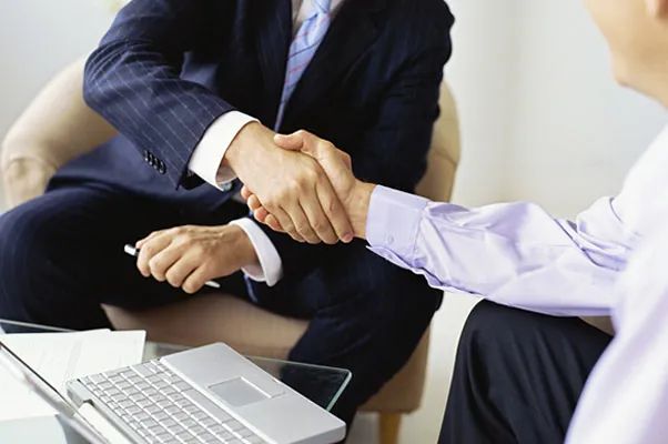 Dos hombres dándose la mano frente a una computadora portátil