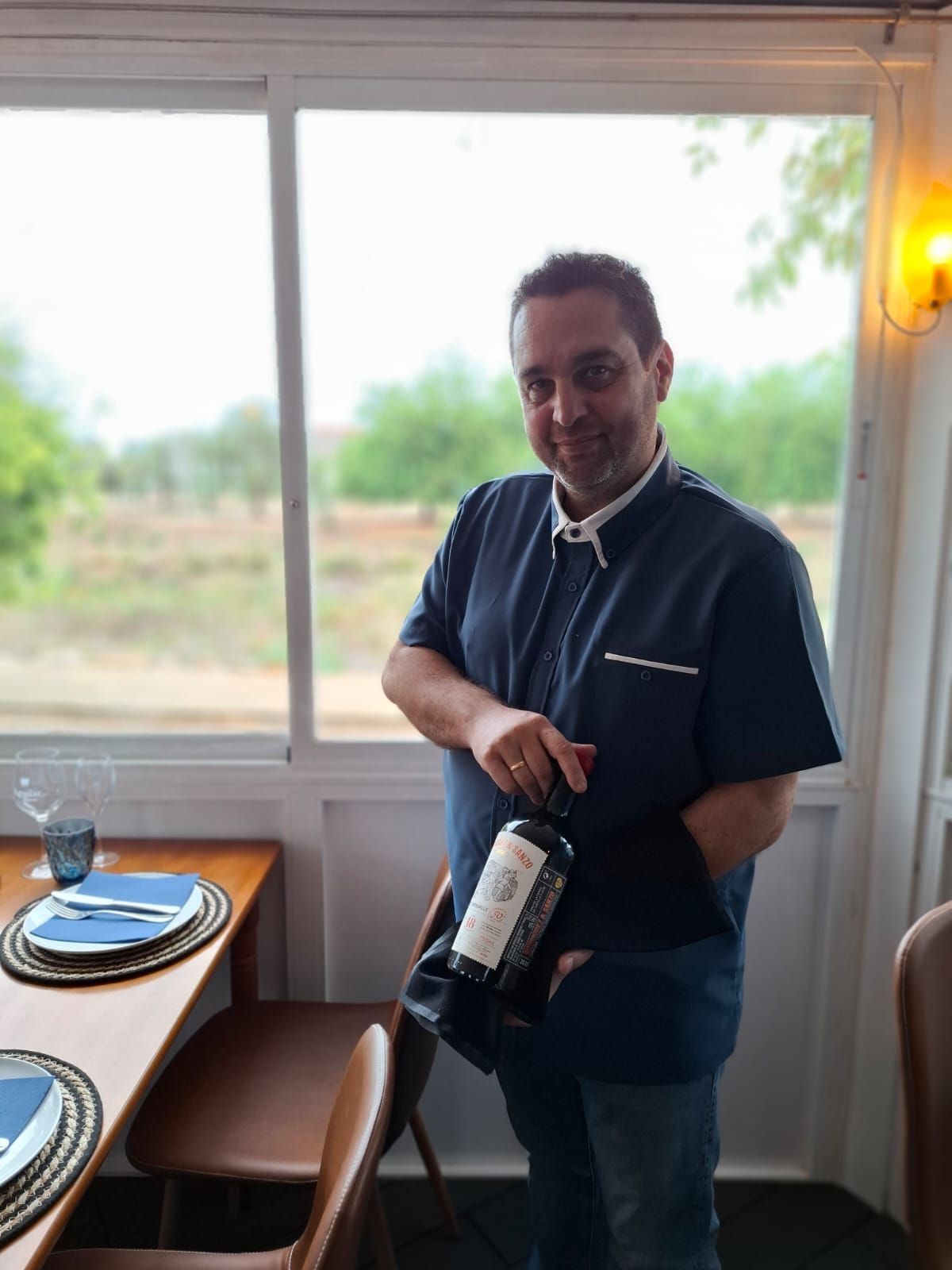 Un hombre con una camisa azul sostiene una botella de vino.