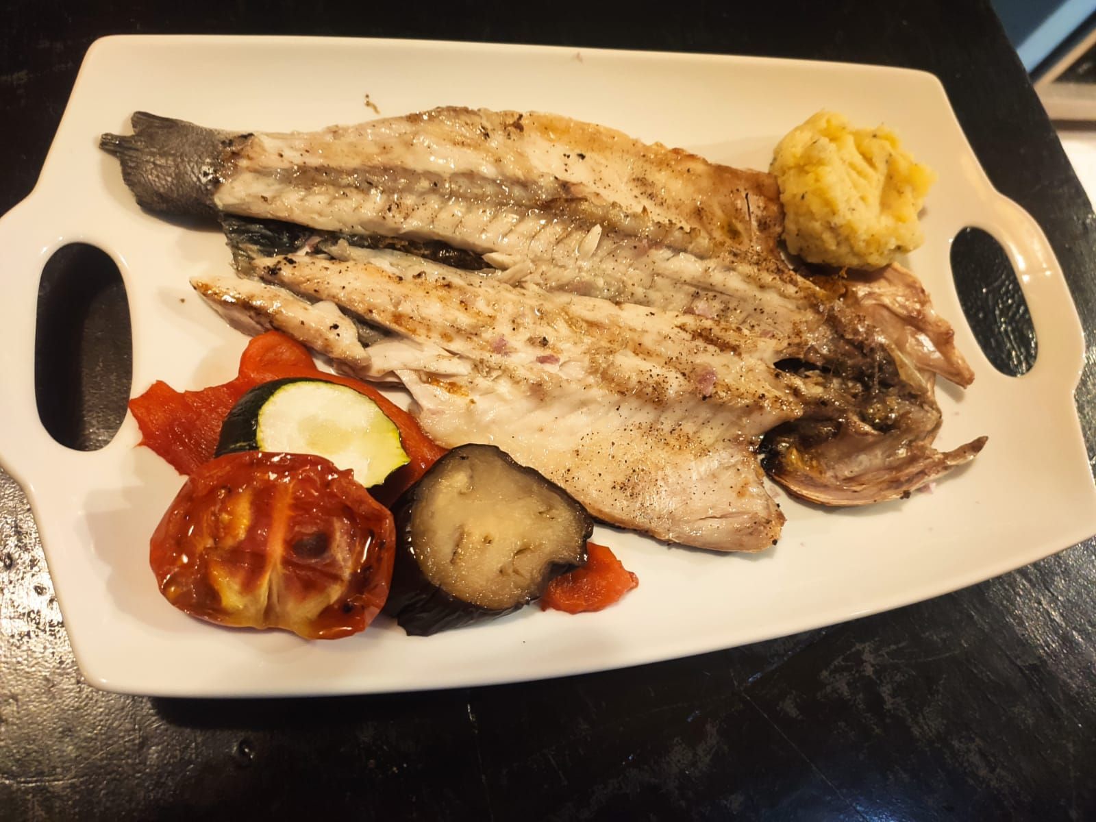 Un plato blanco cubierto con pescado y verduras a la parrilla.
