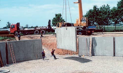 Des ouvriers du bâtiment et une grue installent un grand panneau mural en béton à l'extérieur.