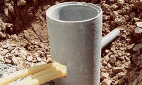 Regard d'égout en béton avec canalisations installées dans une excavation, entourées de terre et de roches.