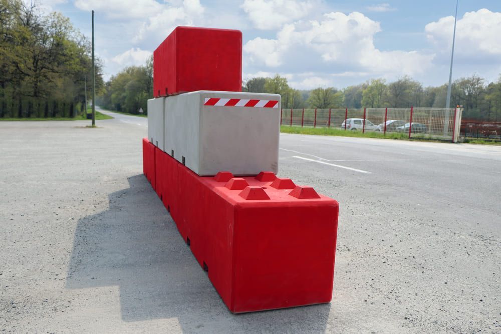 Barrières modulaires en béton rouge et gris le long d'une route, certaines empilées, pour la régulation de la circulation.