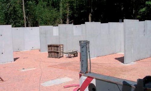 Murs en béton sur une surface gravillonnée avec engins de chantier ; en extérieur.
