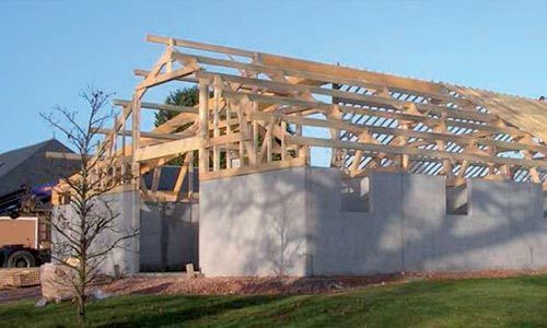 Construction d'une grange à ossature bois sur fondations en béton, en extérieur sous un ciel bleu.