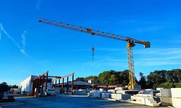 Une grue de chantier jaune surplombe un site de construction avec des matériaux de construction et une structure se détachant sur un ciel bleu.