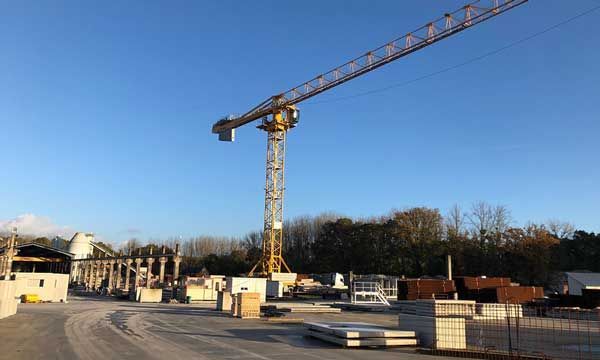 Chantier de construction avec une grue jaune sur fond de ciel bleu. Des bâtiments sont en construction.