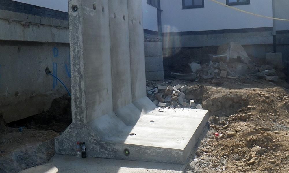 Mur de soutènement en béton en construction. Sections et base en béton gris, avec des gravats dans le sol.