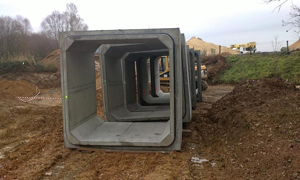 Sections de ponceau en béton empilées en rangée sur un chantier de construction.