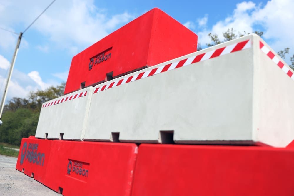 Barrières de sécurité rouges et blanches empilées sur le trottoir, avec des bords rayés en diagonale.