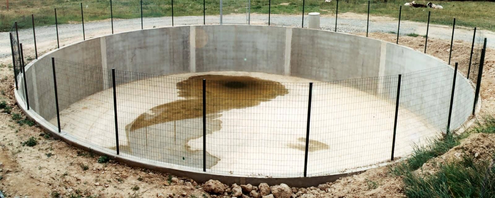 Une structure circulaire en béton contenant de l'eau et entourée de tiges, en extérieur.