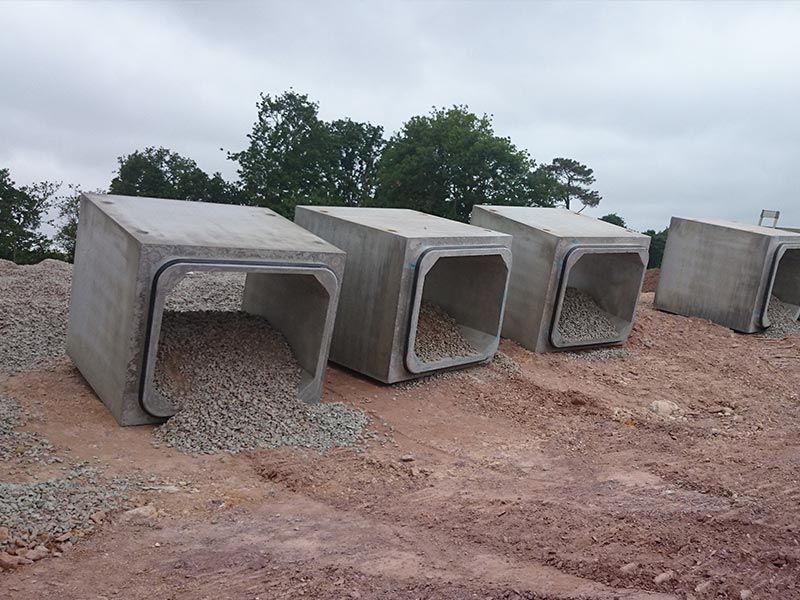 Des ponceaux en béton remplis de gravier sur un chantier de construction, sous un ciel nuageux.