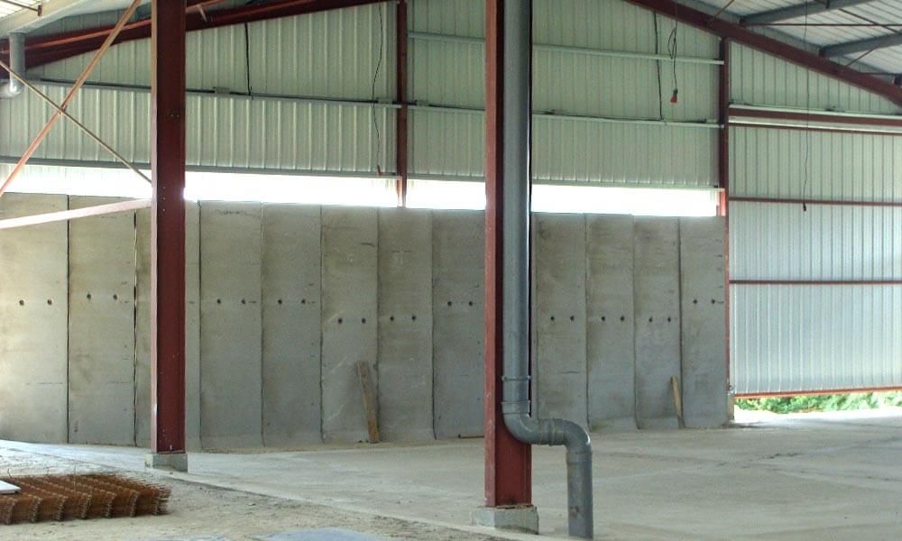 À l'intérieur d'un bâtiment métallique, mur en béton gris, tuyau sombre, structure métallique rouge, sol gris.