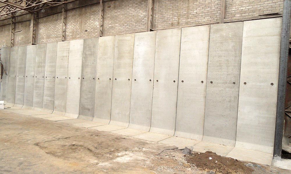 Mur de séparation en béton à l'intérieur d'un entrepôt ; panneaux gris clair reliés par des fixations métalliques.