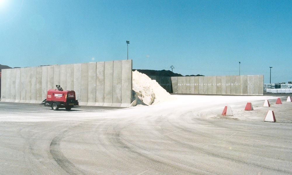 De hauts murs en béton renferment un tas de matériaux blancs. Une machine rouge est garée à proximité.