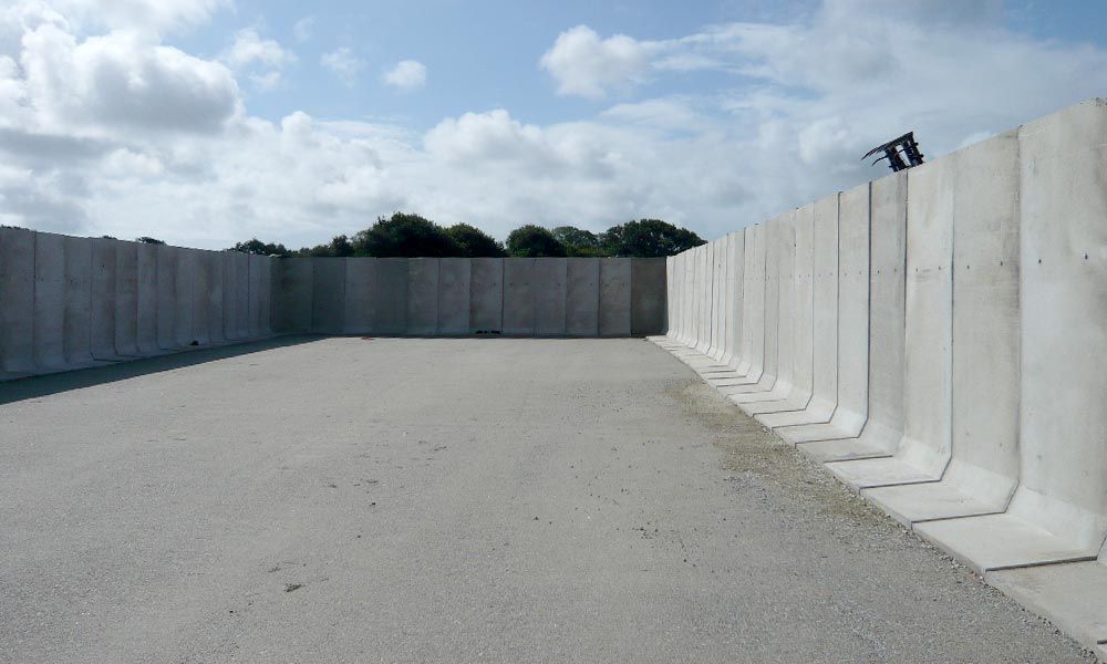 Des murs de béton entourent une aire pavée sous un ciel nuageux.