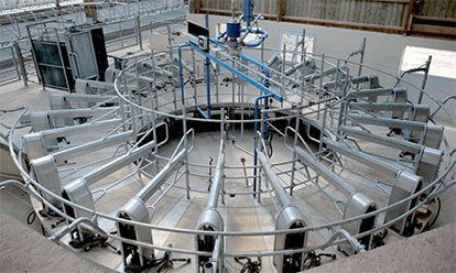Salle de traite circulaire avec bras mécaniques et stalles pour vaches.
