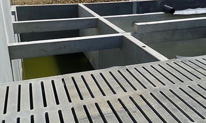 Structure en béton avec passerelle grillagée, poutres de soutien et liquide vert en dessous.