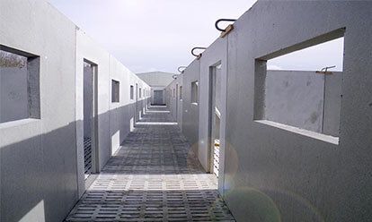 Couloir en béton gris avec des ouvertures rectangulaires. La lumière du soleil projette des ombres sur les murs et le sol à motifs.