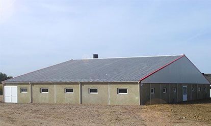 Un long bâtiment industriel bas, au toit gris et aux murs clairs, se détachant sur un ciel bleu.