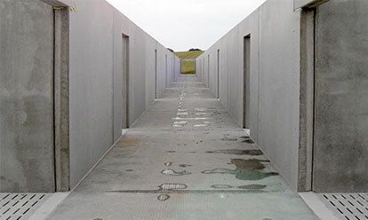 Couloir en béton avec portes, menant à une colline verdoyante au loin.