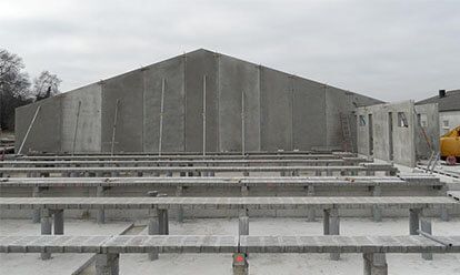 Chantier : murs en béton d’un bâtiment à toit à pignon. Poutres préfabriquées sur fondations.