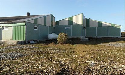 Bâtiments métalliques verts et blancs avec une citerne de propane sur un terrain gravillonné sous un ciel bleu.