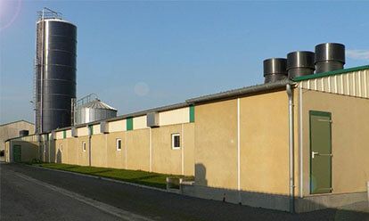 Long bâtiment industriel beige avec un haut silo et des conduits d'aération sous un ciel bleu.
