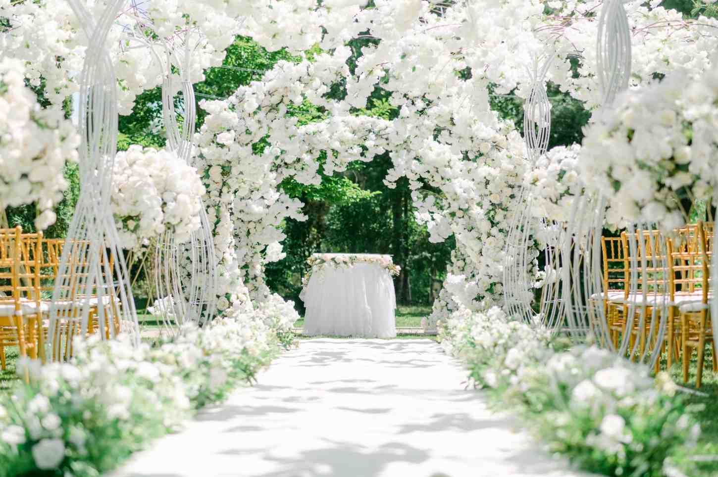 Arco y pasillo con flores blancas para una ceremonia de boda al aire libre.