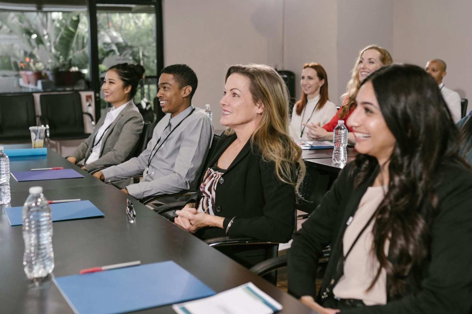 Personas sentadas en una mesa en una sala de conferencias, sonriendo y escuchando.