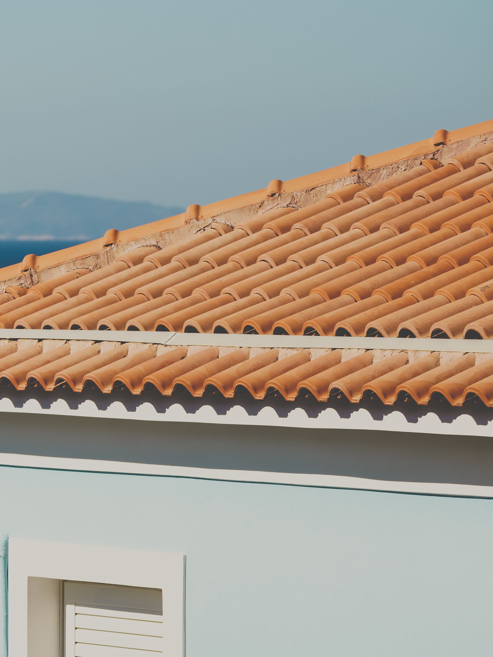 Toit de tuiles orange d'un bâtiment bleu clair avec une fenêtre ; océan et ciel bleu en arrière-plan.