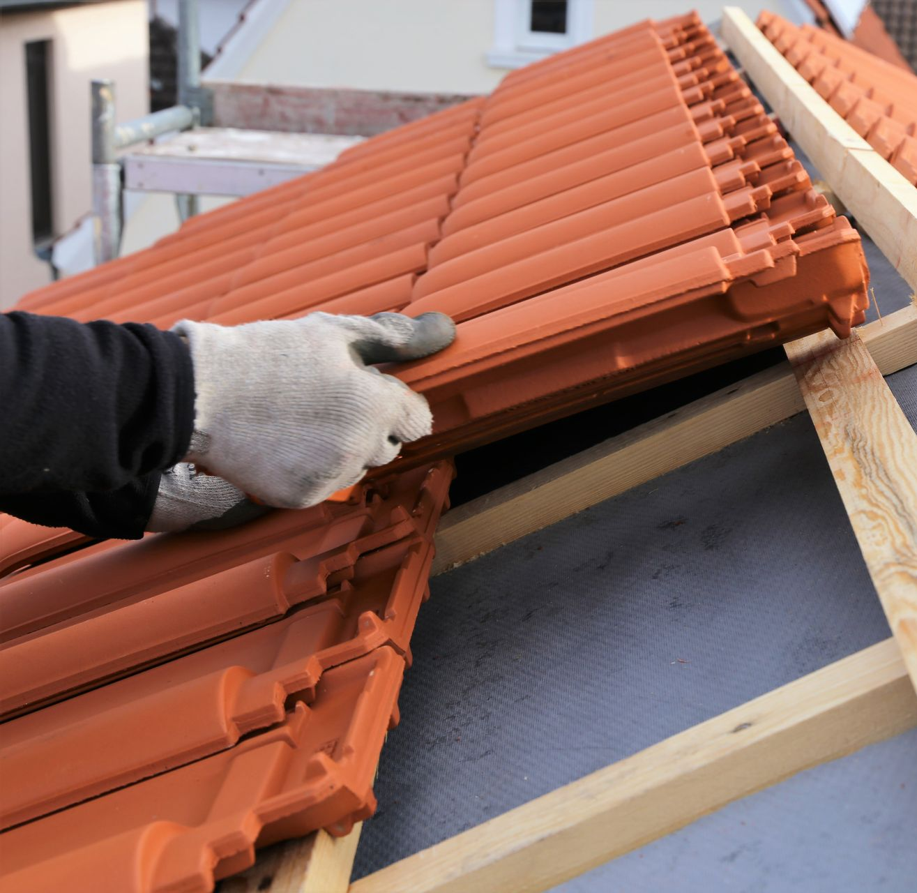 Une personne portant des gants installe des tuiles orange sur une charpente en bois.