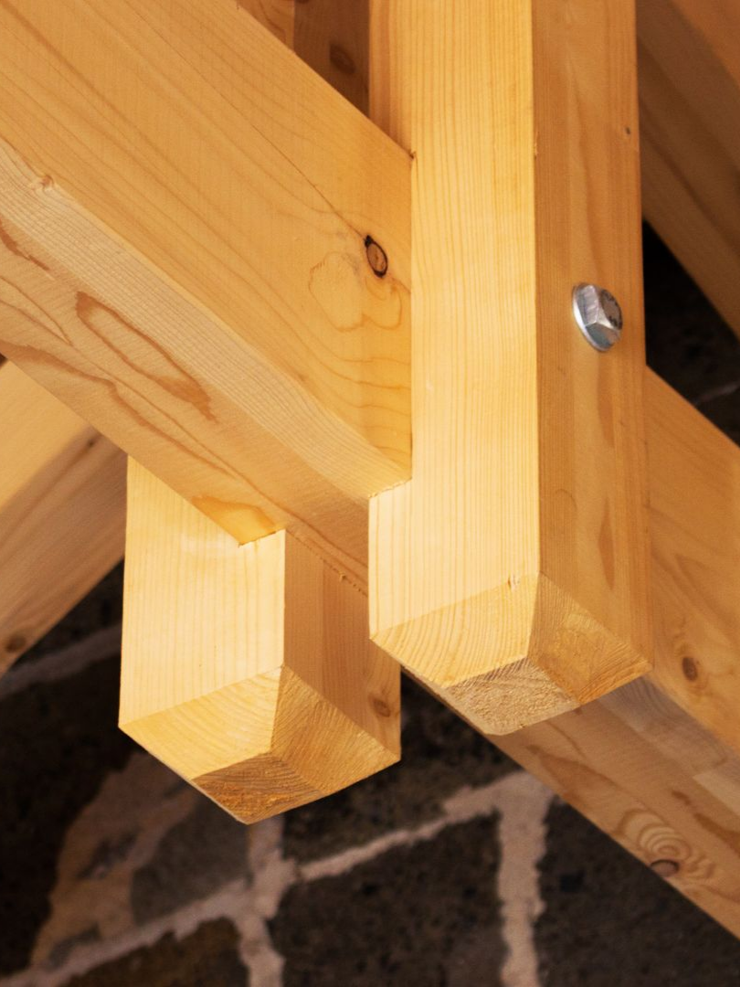 Poutres en bois assemblées par un boulon, faisant partie d'une structure porteuse à extrémités coupées en biseau.