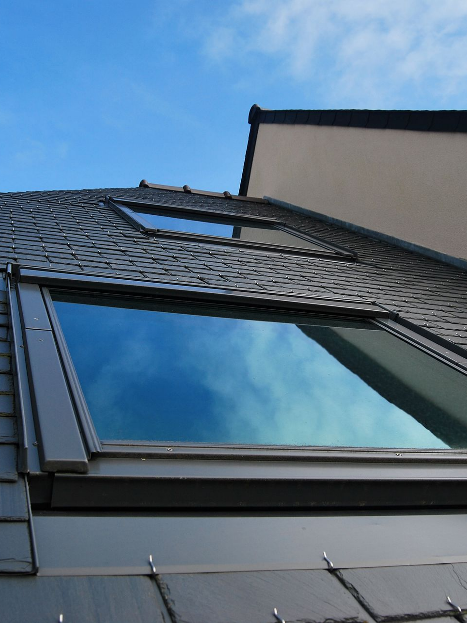 Des puits de lumière dans un toit de bardeaux gris foncé reflètent un ciel d'un bleu éclatant.