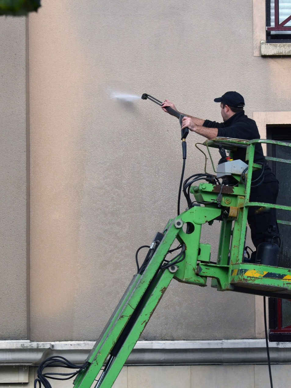 Une personne sur une nacelle lave l'extérieur du bâtiment au nettoyeur  à haute pression.