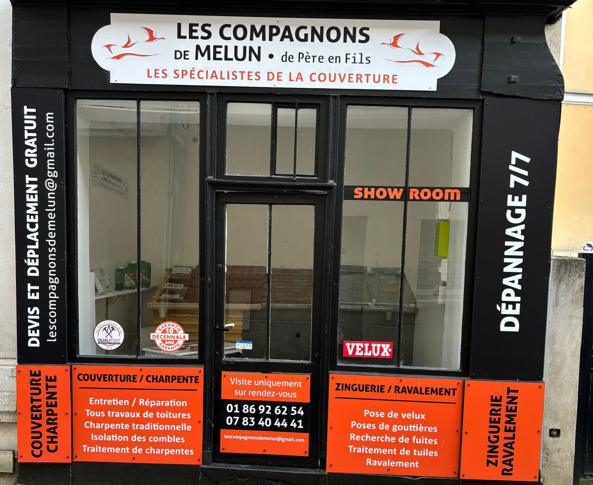 Façade du magasin Les Compagnons de Melun avec services de toiture. Façade sombre, touches d'orange.