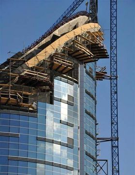 Edificio de gran altura en construcción con andamios y pisos superiores expuestos contra el cielo azul.